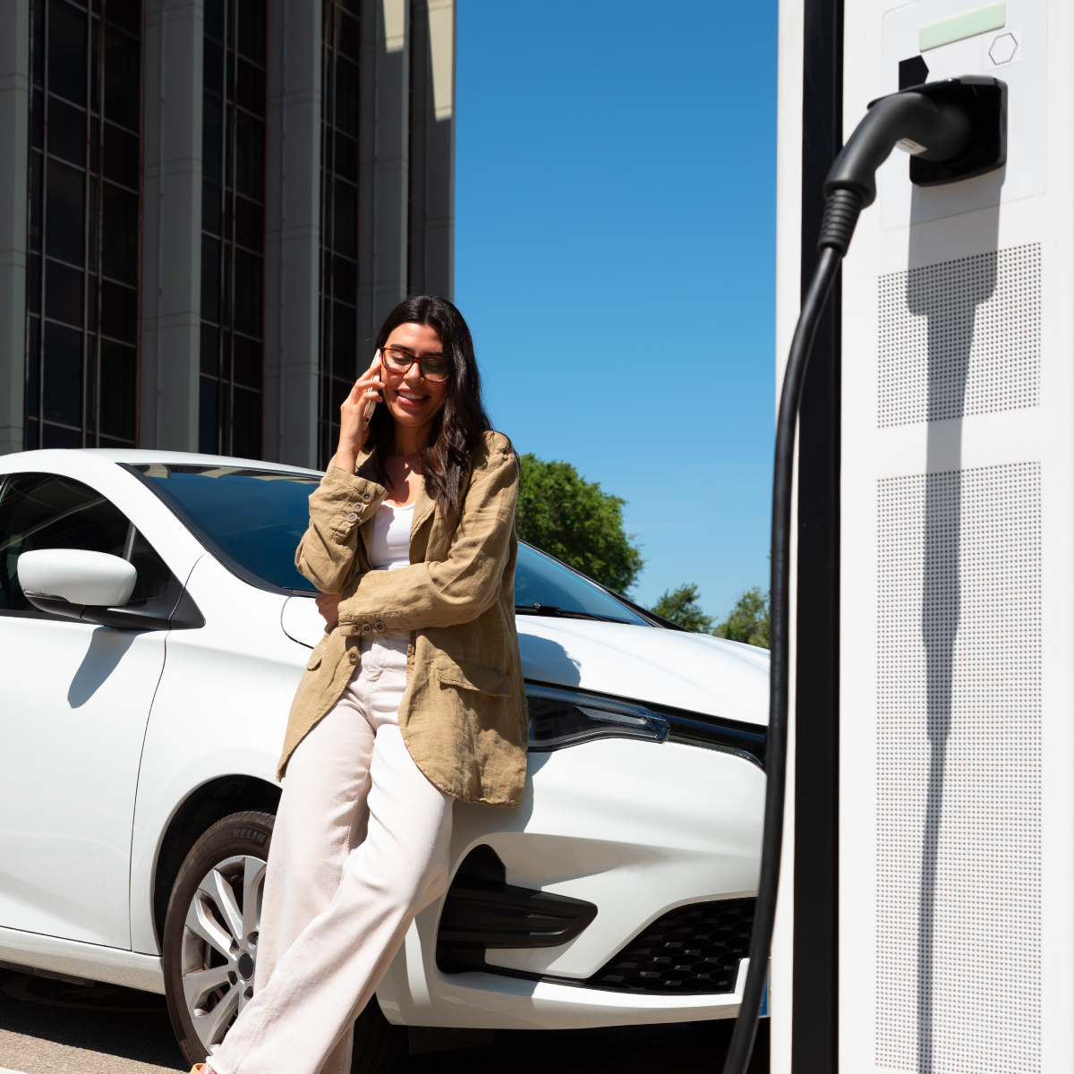 Jeune femme qui attend que sa voiture électrique se recharge avec une borne de chargement au premier plan